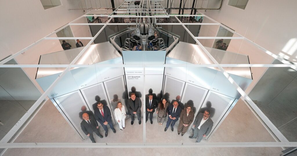 Quantencomputer IBM Quantum System Two von oben, davor eine Gruppe von Menschen