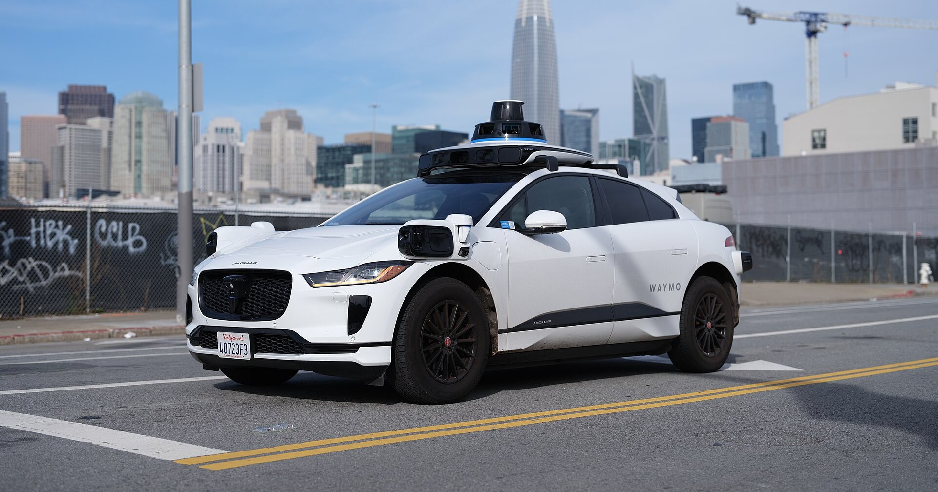Weisser Jaguar I-Pace von Waymo mit Sensoren auf dem Dach vor der Skyline von San Francisco