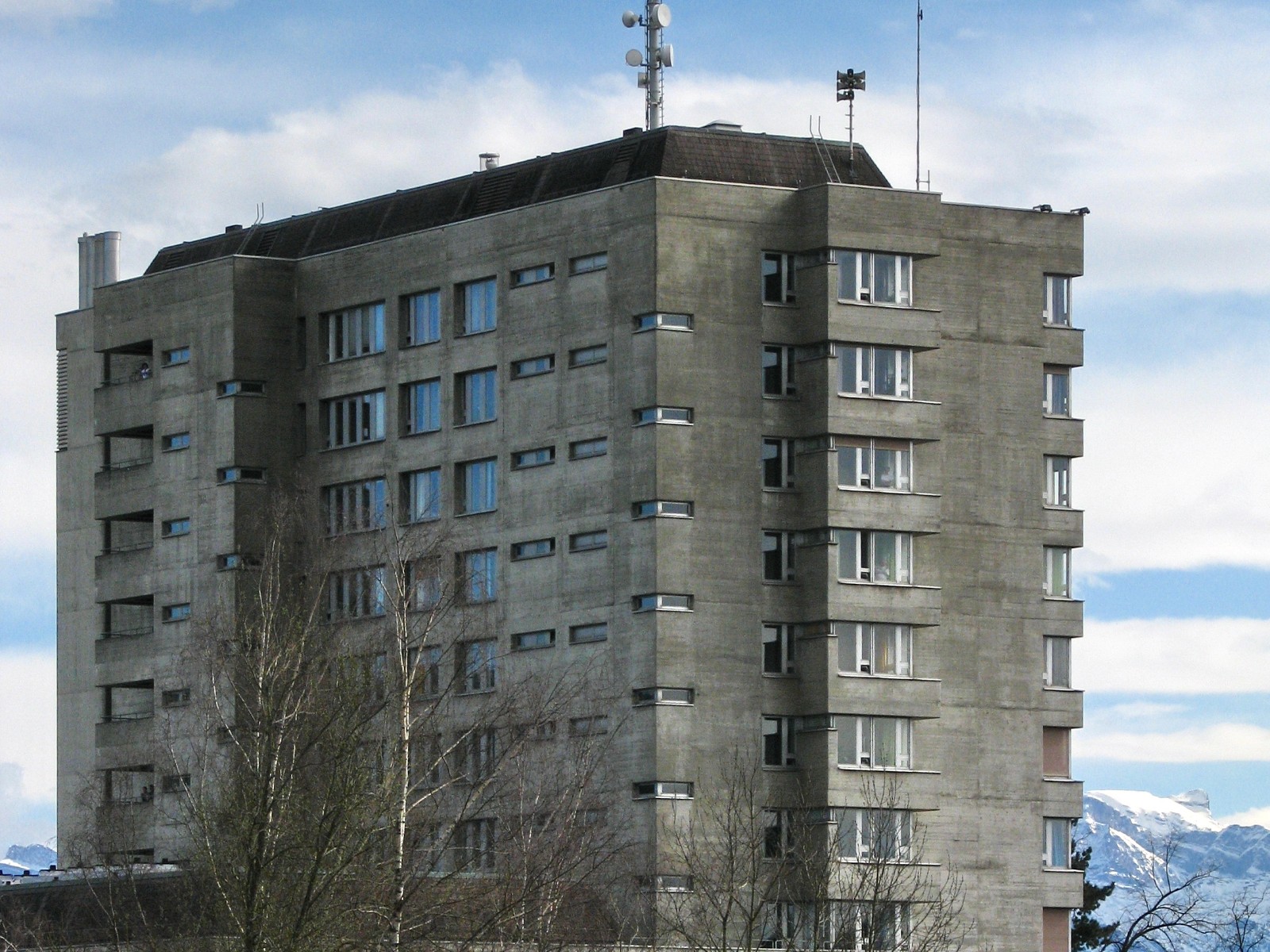 Das Hochhaus des GZO Spitals Wetzikon an der Spitalstrasse, davor Bäume, im Hintergrund die Alpen.